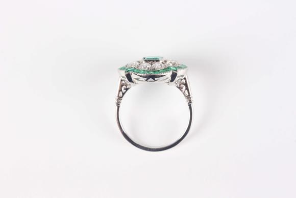 TooveysA platinum, emerald and diamond ring in an Art Deco inspired cluster design, mounted with the cut cornered rectangular step cut emerald within a quatr