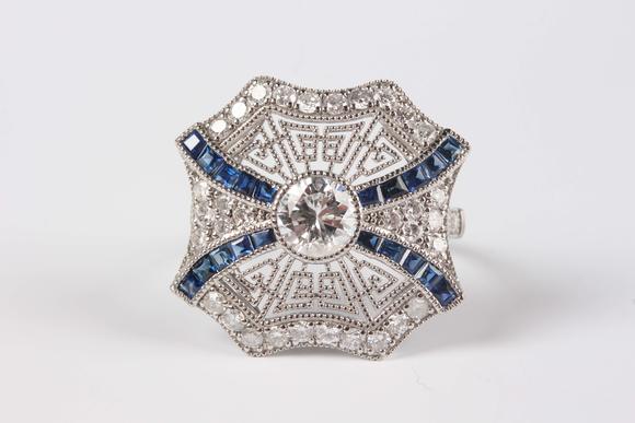 TooveysA platinum, sapphire and diamond ring, collet set with the principal circular cut diamond at the centre, otherwise in a pierced millegrain design, det