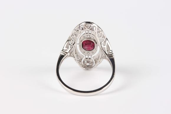 TooveysA platinum, ruby and diamond oval ring in an Art Deco inspired design, collet set with the oval cut ruby at the centre, detailed ‘Pt950’, weight 4.5
