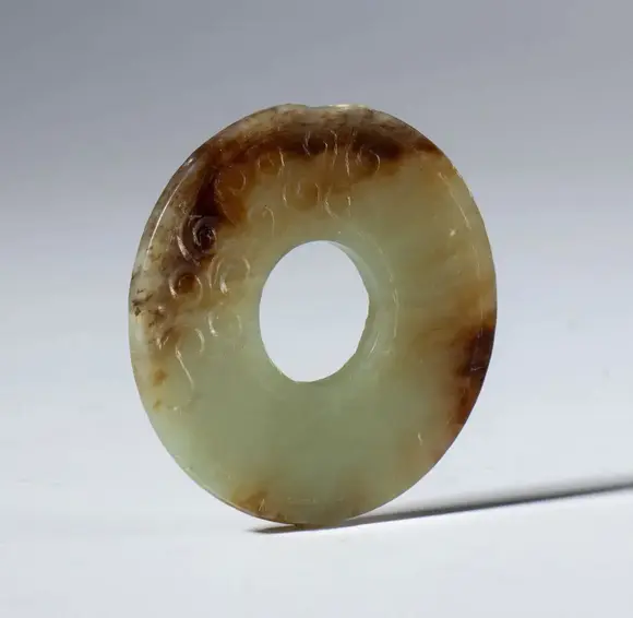 Bertolami Fine ArtA beautiful Bi disk in transparent jade with dark hues and small spiral carvings. China, Qing Dynasty (1644-1912), late 19th century.