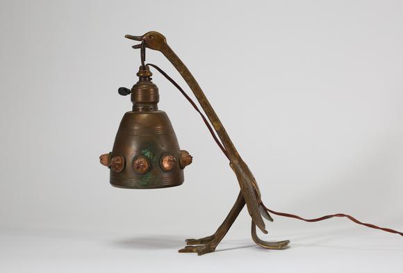 Goldfield Auction sarlsLampe de table Art déco en métal patiné figurant un échassier stylisé soutenant une bobèche suspendue, ornée de cabochons en relief. Travail des année