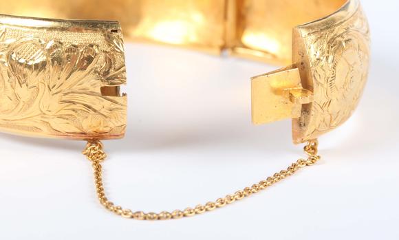 TooveysA gold circular hinged bangle with floral engraved decoration, on a