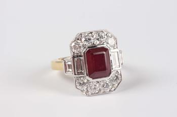 An 18ct two colour gold, ruby and diamond cluster ring, collet set with the cut cornered rectangular step cut ruby within a surround of baguette and c