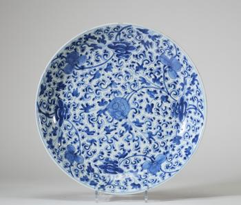 Plat en porcelaine bleu et blanc, Chine, à décor dense de rinceaux fleuris et pivoines stylisées de l’époque Kangxi, l’aile extérieure ornée de bran