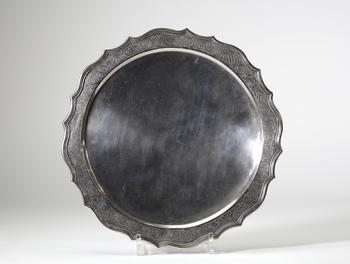 Assiette dite volante en argent massif, travail liégeois daté 1724, de forme circulaire à bord contourné et légèrement festonné. Elle repose sur trois